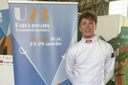 Junger Fechter in wei&szlig;er Ausr&uuml;stung steht neben einem Banner f&uuml;r die U23 Europameisterschaften 2026.