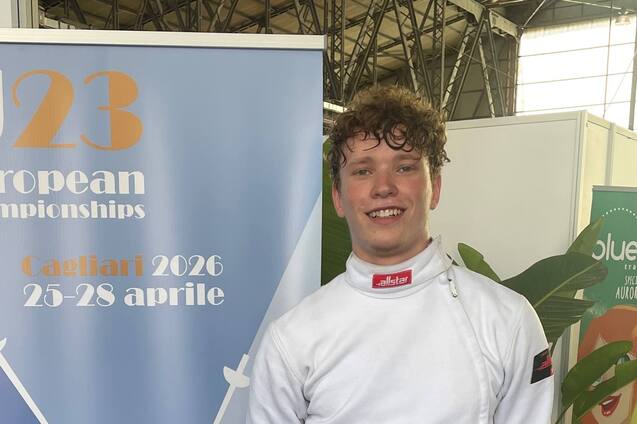 Junger Fechter in Wettkampfuniform steht neben einem Banner der U23 Europameisterschaften 2026 in Cagliari.