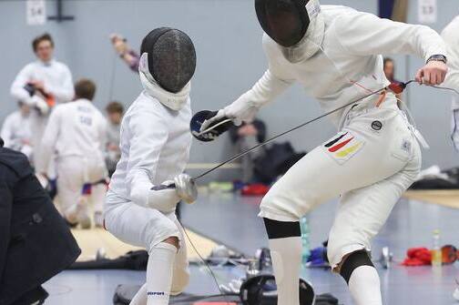 Zwei Fechter in Vollmontur k&auml;mpfen auf einer Wettkampfmatte in einer Sporthalle.