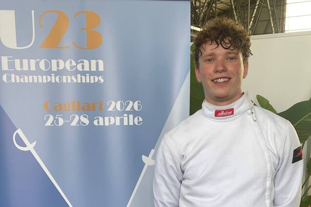 Junger Fechter in Wettkampfuniform steht neben einem Banner der U23 Europameisterschaften 2026 in Cagliari.
