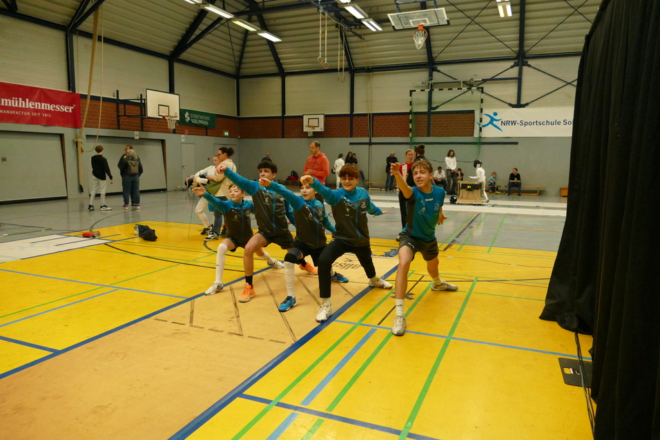 Gruppe von Jugendlichen in Sportkleidung, die eine gemeinsame &Uuml;bung in einer Sporthalle durchf&uuml;hren.