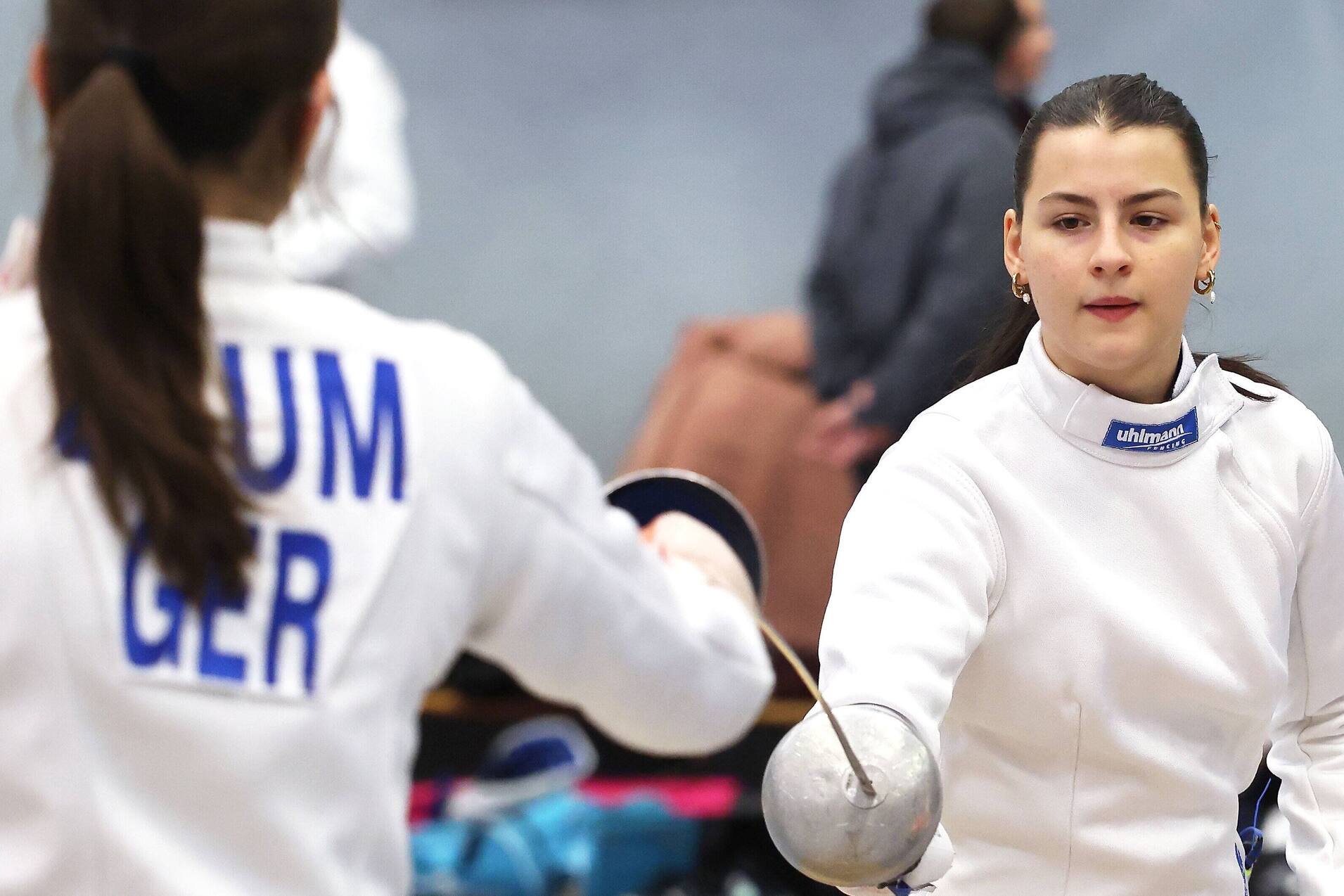 Zwei Fechterinnen in sportlicher Ausr&uuml;stung absolvieren ein Training in einer Turnhalle.