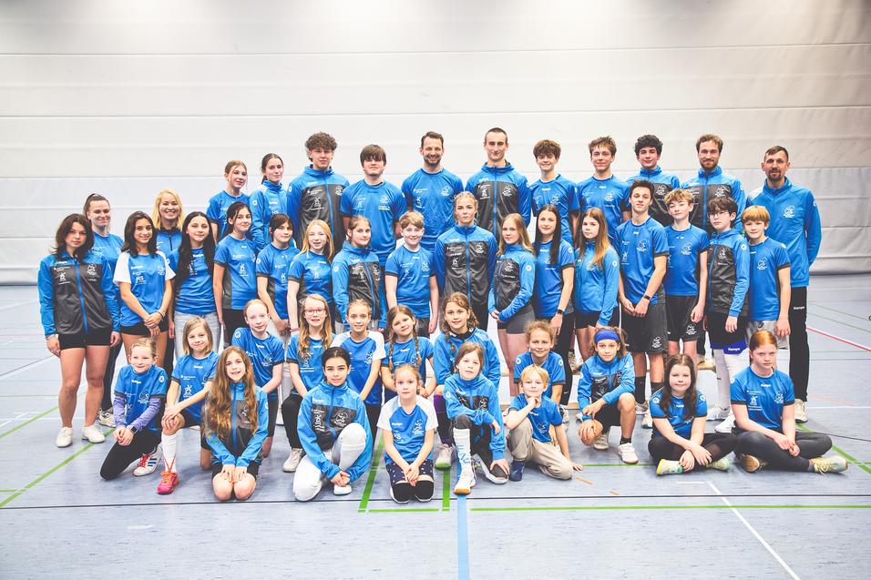 Gruppenfoto einer Sportmannschaft in blauen Trikots, bestehend aus Kindern und Jugendlichen in einer Sporthalle.