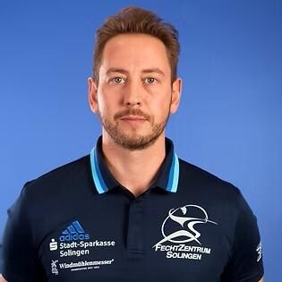 Portr&auml;t eines Mannes mit kurzen Haaren, getragenem Polo-Shirt des Fechtzentrums Solingen, vor blauem Hintergrund.