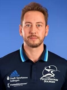 Portr&auml;t eines Mannes mit kurzen Haaren, getragenem Polo-Shirt des Fechtzentrums Solingen, vor blauem Hintergrund.