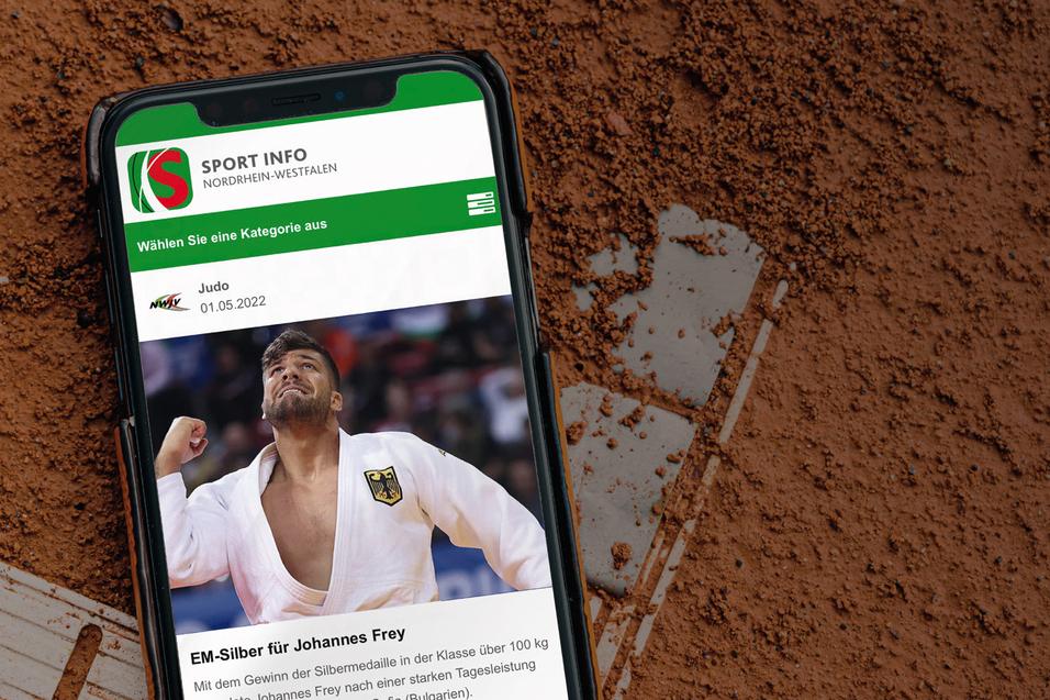Smartphone mit Sportnews &uuml;ber Johannes Frey auf einem Hintergrund aus rotem Sand, wahrscheinlich von einem Tennisplatz.