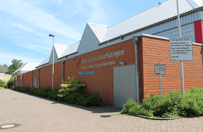Fassade der NRW Sportschule Solingen mit Zugang zur Friedrich-Albert-Lange-Sporthalle und Pflanzen im Vordergrund.