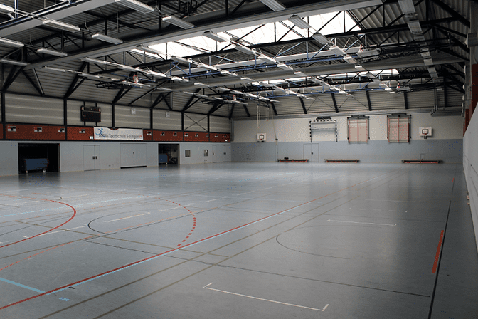 Große Sporthalle mit hellem Boden, Basketballkörben und markierten Spielfeldern.